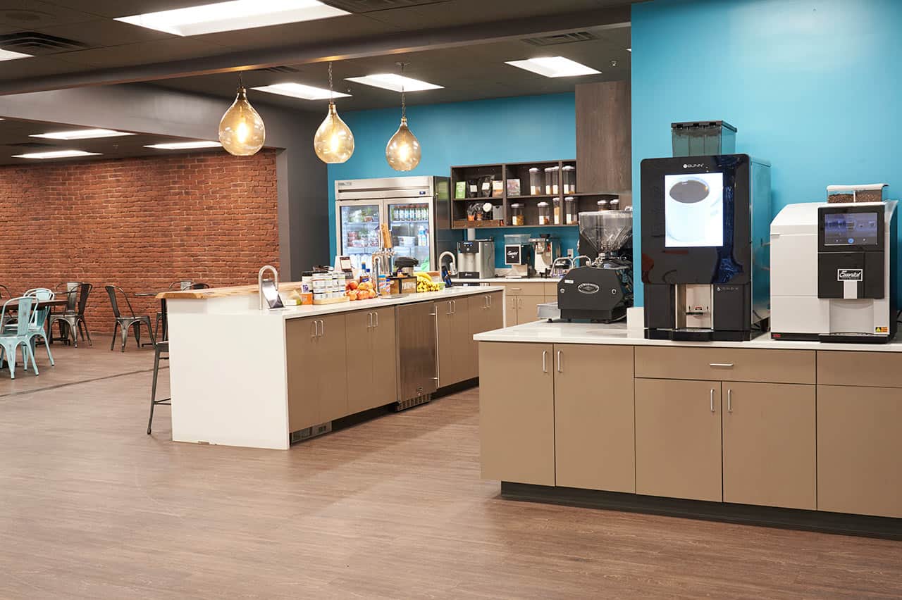 Open concept office kitchen with modern amenities such as a espresso machine and industrial fridge