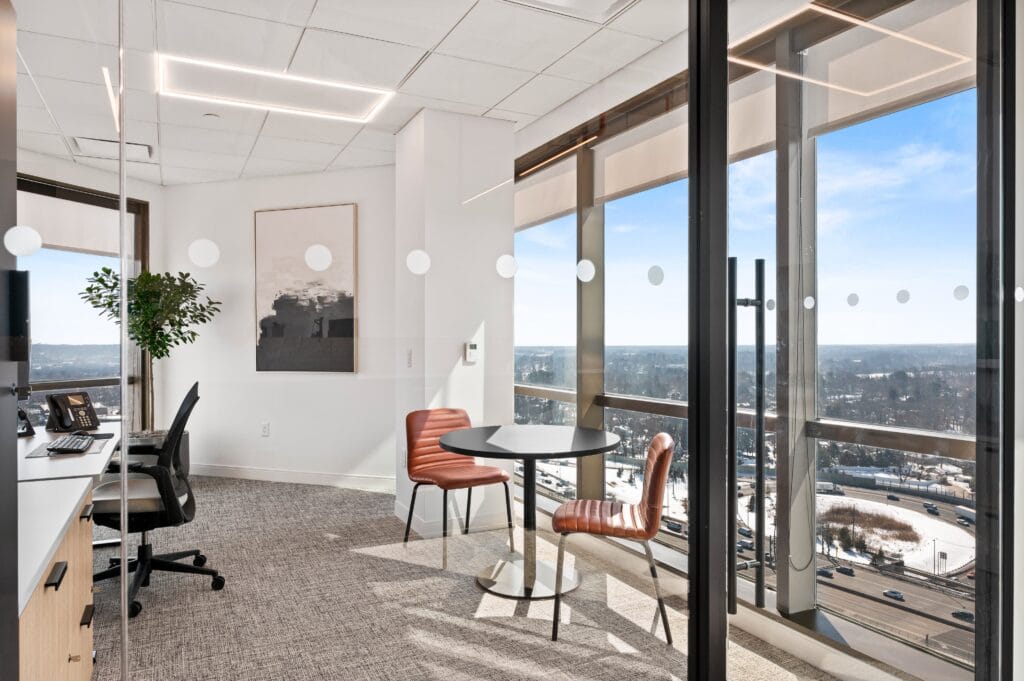 Window office at LS Power workplace retreat in East Brunswick, with workstation, round meeting table, and floor-to-ceiling exterior views